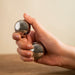 Medium Baoding balls with chimes in a woman's hand against a wooden table.  These chrome Baoding balls are great for arthritic hands or carpal tunnel.  Hand care products.