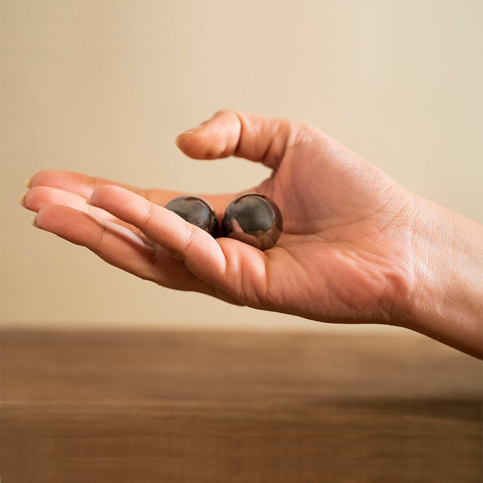 Small solid Baoding balls in a woman's hand against a wooden table. These steel Baoding balls are great for arthritic hands or carpal tunnel.